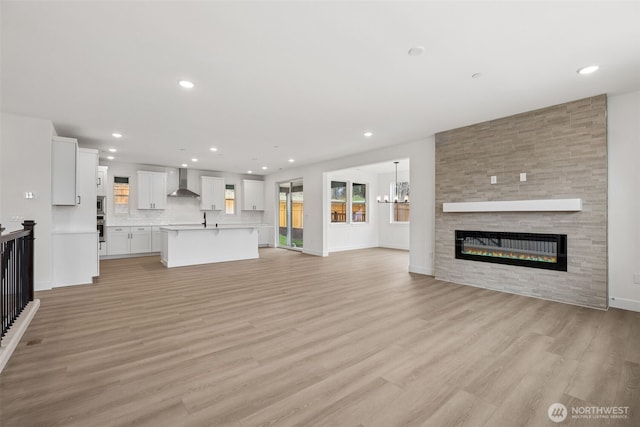 unfurnished living room with baseboards, light wood finished floors, recessed lighting, a fireplace, and a chandelier