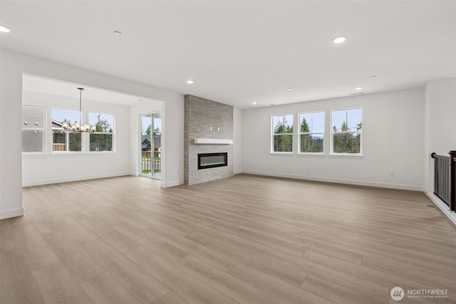 unfurnished living room with baseboards, a chandelier, light wood-type flooring, recessed lighting, and a fireplace