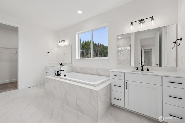 bathroom with marble finish floor, vanity, and a garden tub