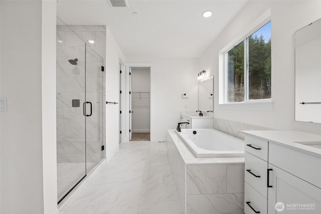 bathroom with a walk in closet, two vanities, marble finish floor, a shower stall, and a bath