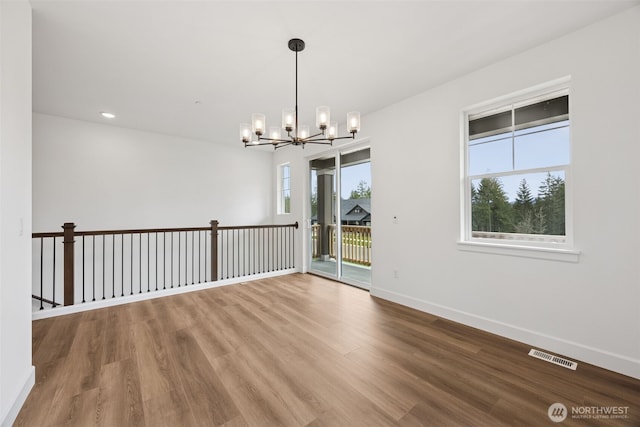 spare room with a notable chandelier, visible vents, baseboards, and wood finished floors