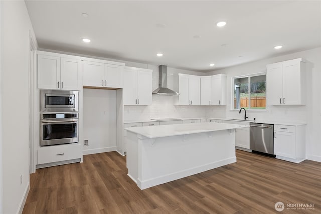 kitchen featuring a sink, stainless steel appliances, dark wood-type flooring, wall chimney exhaust hood, and a center island