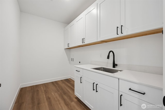 clothes washing area with baseboards, cabinet space, a sink, washer hookup, and dark wood-type flooring