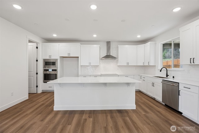 kitchen featuring a kitchen island, dark wood-style flooring, a sink, appliances with stainless steel finishes, and wall chimney exhaust hood