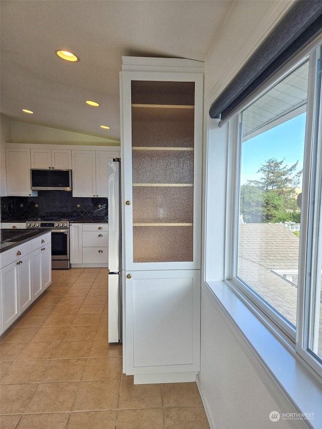 kitchen featuring backsplash, vaulted ceiling, light tile patterned flooring, white cabinetry, and stainless steel appliances