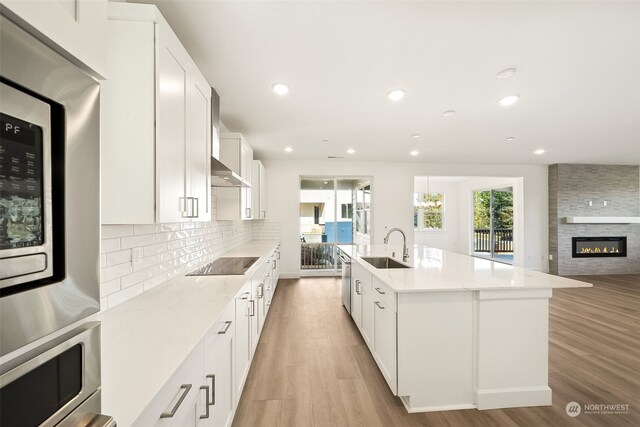 kitchen with white cabinetry, black electric stovetop, light stone countertops, and a center island with sink