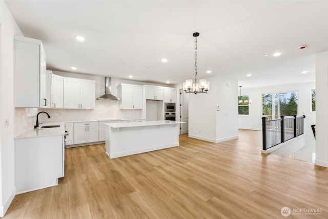 kitchen with light wood finished floors, a sink, light countertops, wall chimney exhaust hood, and a center island