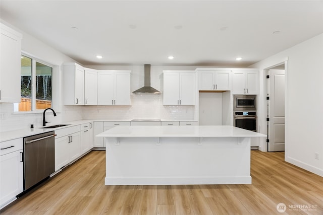 kitchen featuring a sink, stainless steel appliances, wall chimney exhaust hood, and light wood finished floors