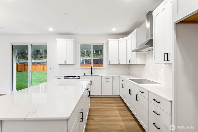 kitchen featuring a sink, light stone counters, light wood-style floors, wall chimney range hood, and black electric stovetop