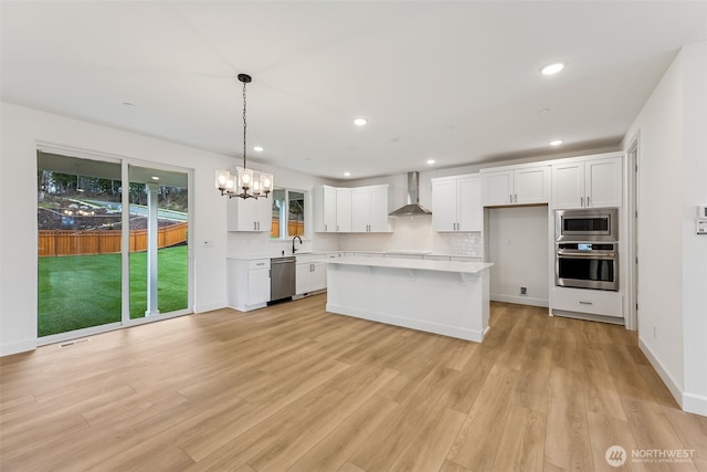 kitchen featuring stainless steel appliances, light countertops, white cabinets, wall chimney exhaust hood, and backsplash