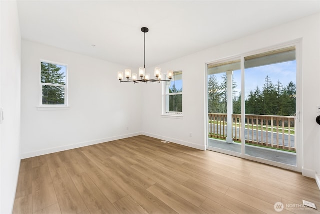 unfurnished dining area with plenty of natural light, baseboards, an inviting chandelier, and wood finished floors