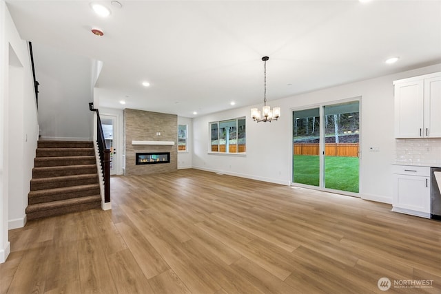 unfurnished living room featuring stairway, an inviting chandelier, recessed lighting, a fireplace, and light wood-type flooring