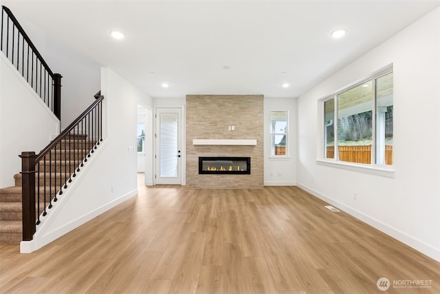 unfurnished living room featuring light wood finished floors, baseboards, a tiled fireplace, stairway, and recessed lighting