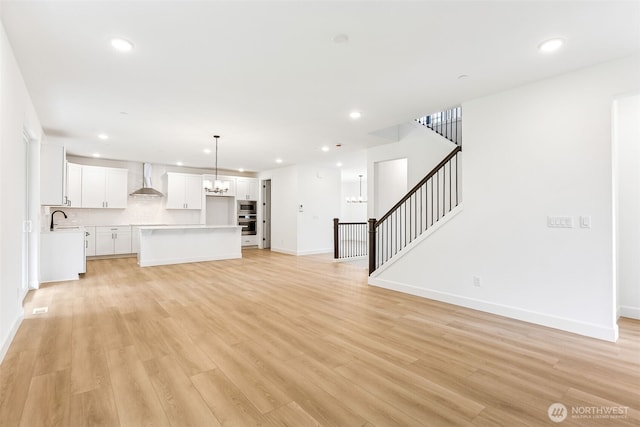 unfurnished living room with light wood-type flooring, stairs, an inviting chandelier, and a sink