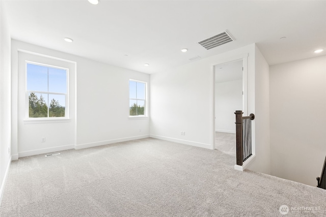 empty room with a healthy amount of sunlight, visible vents, and light carpet