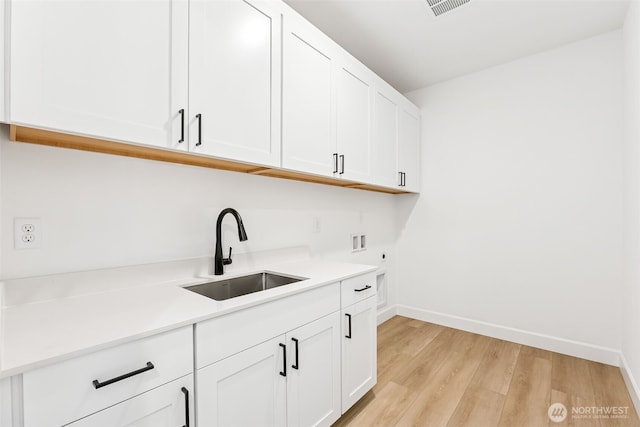 kitchen with a sink, white cabinetry, light wood finished floors, baseboards, and light countertops