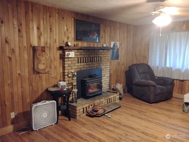 living room featuring a wood stove, wood walls, light hardwood / wood-style flooring, and ceiling fan