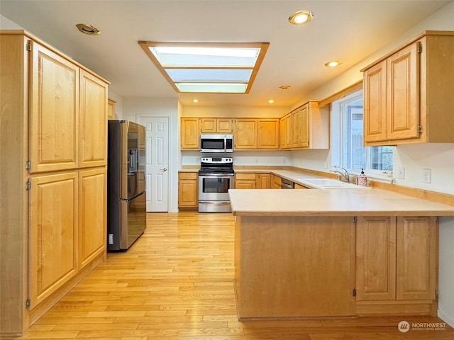 kitchen featuring kitchen peninsula, appliances with stainless steel finishes, light brown cabinetry, a skylight, and light hardwood / wood-style floors