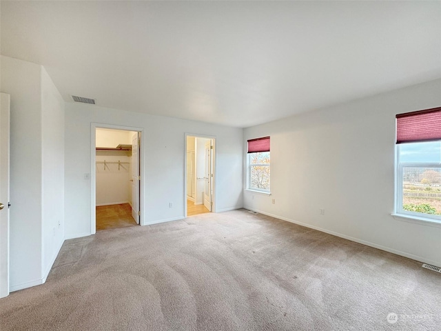 unfurnished bedroom with light colored carpet, a walk in closet, and a closet