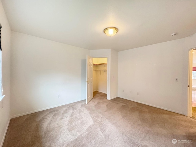 unfurnished bedroom featuring light carpet, a walk in closet, and a closet