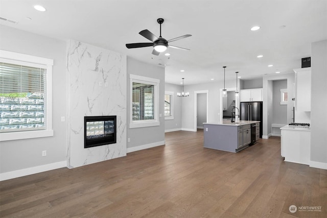 kitchen with dark wood-type flooring, a center island with sink, white cabinets, a premium fireplace, and decorative light fixtures