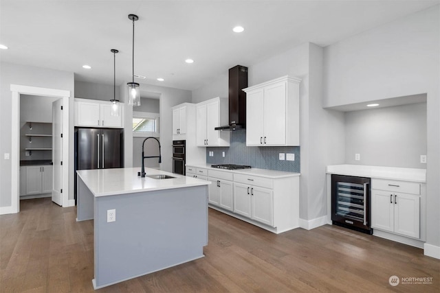 kitchen with appliances with stainless steel finishes, beverage cooler, sink, wall chimney range hood, and hanging light fixtures