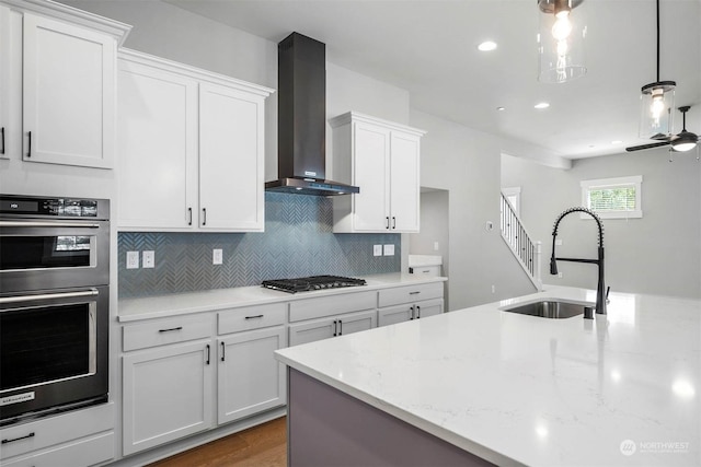 kitchen with appliances with stainless steel finishes, wall chimney exhaust hood, sink, decorative light fixtures, and white cabinets