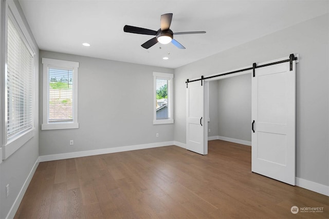 unfurnished bedroom with a barn door, ceiling fan, and wood-type flooring