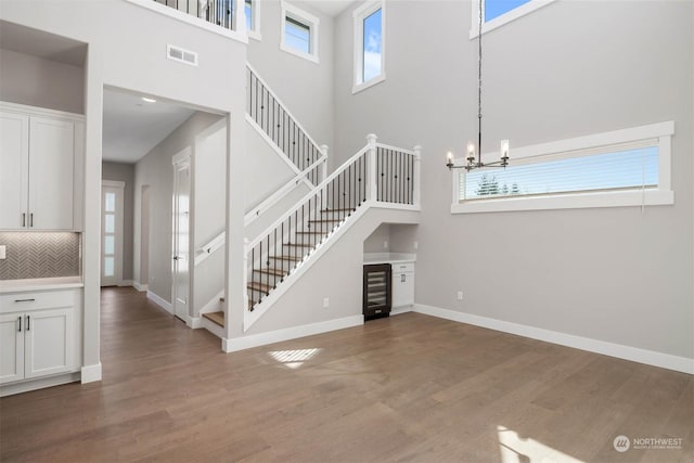 unfurnished living room featuring a high ceiling, dark hardwood / wood-style flooring, an inviting chandelier, and beverage cooler