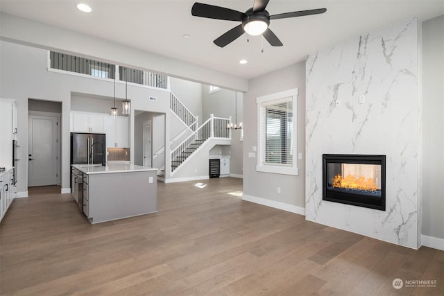 kitchen with white cabinets, a premium fireplace, an island with sink, decorative light fixtures, and wood-type flooring