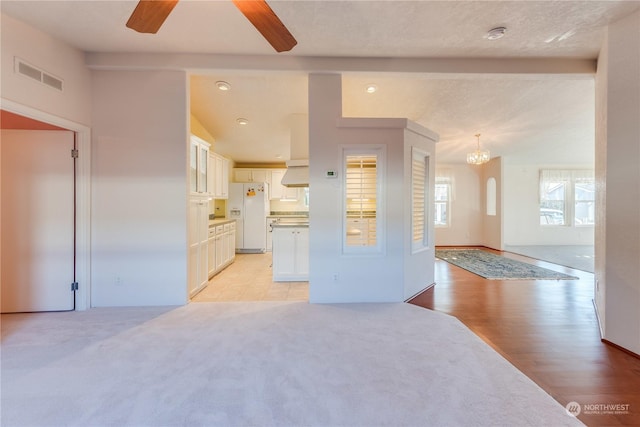 living room with ceiling fan with notable chandelier, light hardwood / wood-style floors, and a textured ceiling