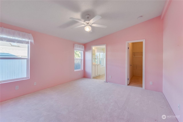 unfurnished bedroom featuring lofted ceiling, ceiling fan, a spacious closet, connected bathroom, and a closet