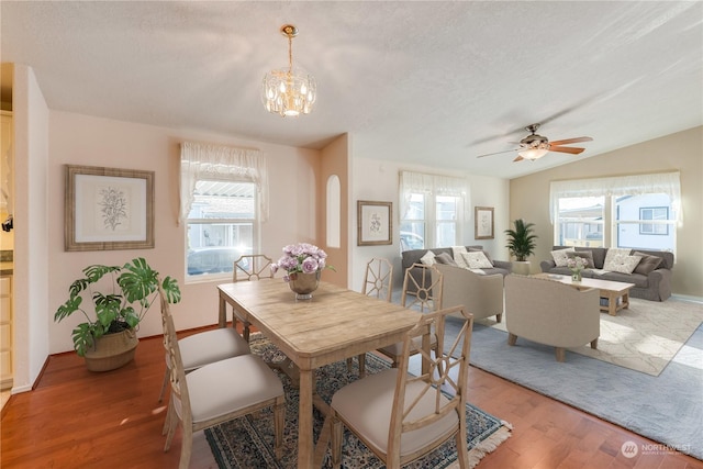 dining area with a textured ceiling, ceiling fan with notable chandelier, wood-type flooring, and vaulted ceiling