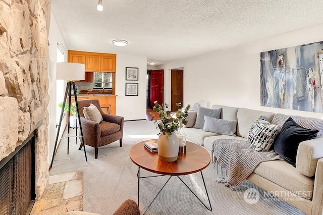 living room with a stone fireplace, light colored carpet, and a textured ceiling