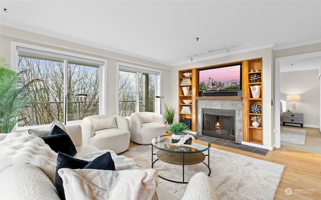 living room featuring a tiled fireplace, hardwood / wood-style flooring, track lighting, and ornamental molding