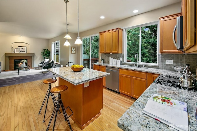 kitchen with light wood finished floors, appliances with stainless steel finishes, open floor plan, a sink, and a kitchen island