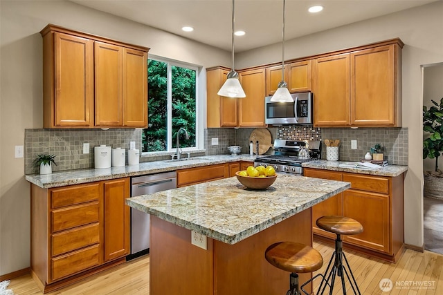 kitchen featuring a center island, appliances with stainless steel finishes, light wood-style floors, a sink, and a kitchen bar