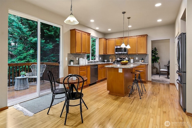 kitchen with light wood-style floors, appliances with stainless steel finishes, brown cabinets, and a center island