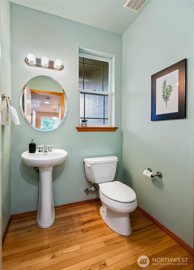 half bath with baseboards, visible vents, toilet, and wood finished floors