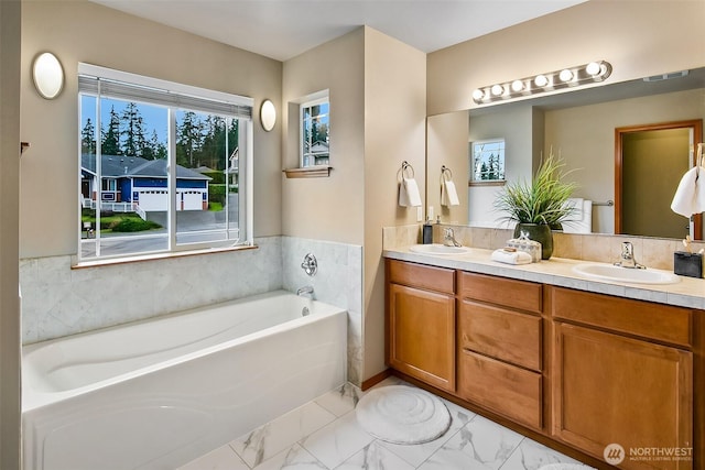 full bathroom with marble finish floor, double vanity, a sink, and a bath