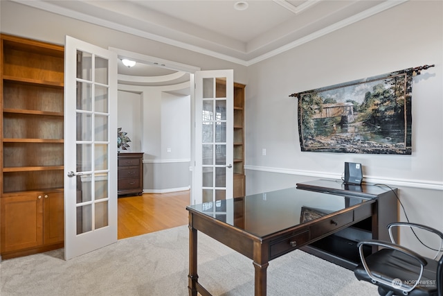 office space featuring ornamental molding, light hardwood / wood-style flooring, a tray ceiling, and french doors