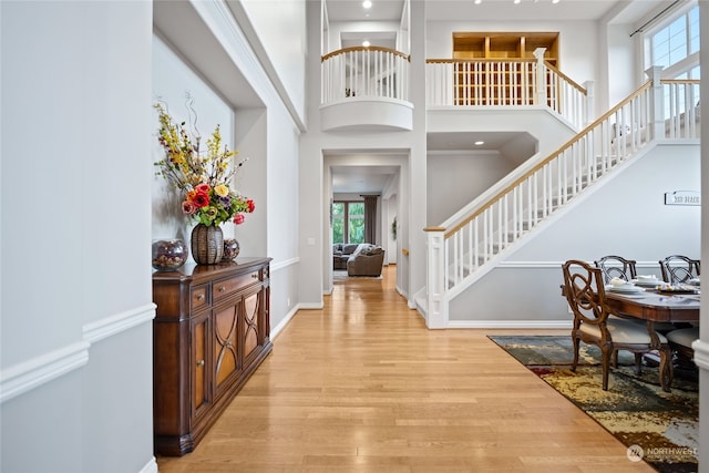 entrance foyer with crown molding, light hardwood / wood-style flooring, and a towering ceiling