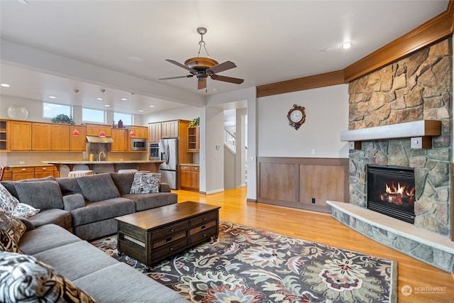 living room featuring a stone fireplace, ceiling fan, sink, and light hardwood / wood-style floors