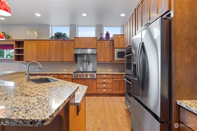 kitchen featuring light stone countertops, sink, stainless steel appliances, backsplash, and light wood-type flooring