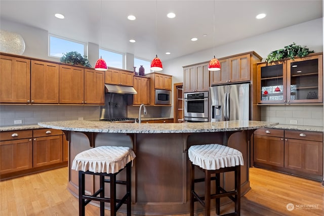 kitchen featuring pendant lighting, a breakfast bar, light wood-type flooring, light stone counters, and stainless steel appliances