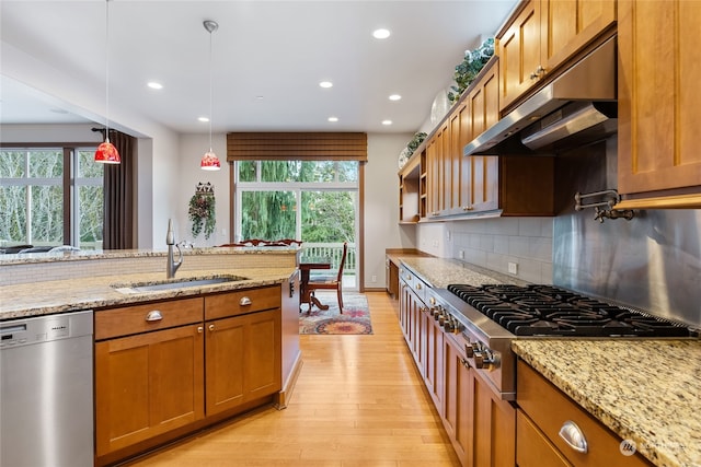 kitchen with light stone countertops, appliances with stainless steel finishes, sink, light hardwood / wood-style floors, and hanging light fixtures