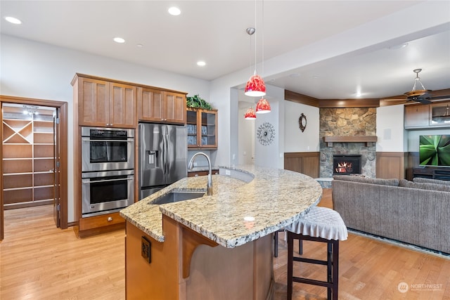 kitchen featuring appliances with stainless steel finishes, light wood-type flooring, sink, a stone fireplace, and hanging light fixtures