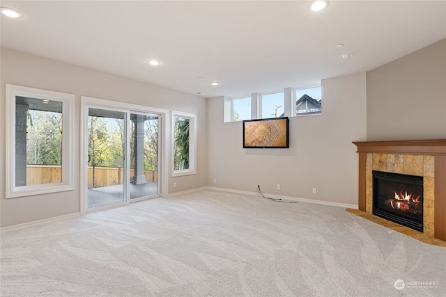 unfurnished living room with a tile fireplace, light carpet, and a wealth of natural light