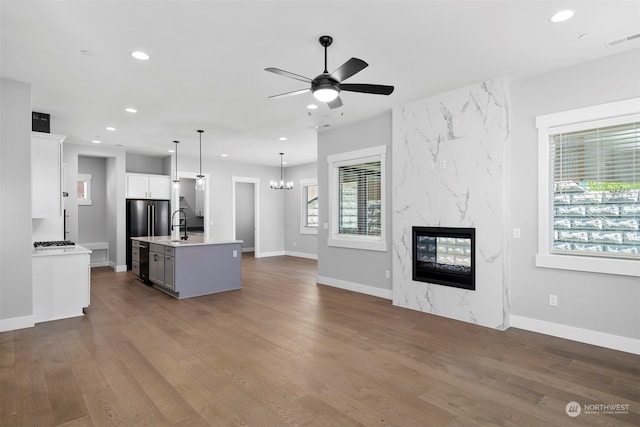 kitchen with pendant lighting, a center island with sink, a fireplace, white cabinetry, and wood-type flooring