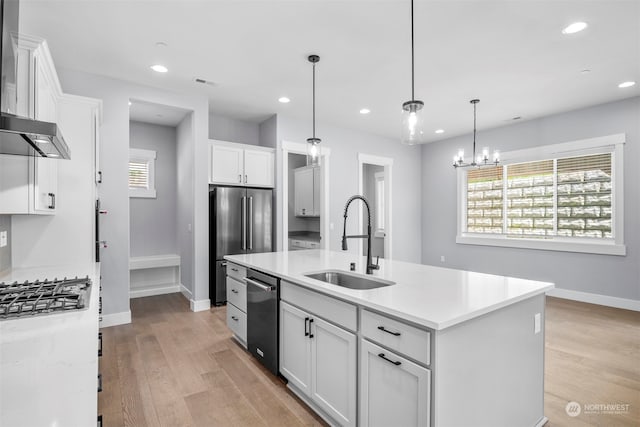 kitchen featuring white cabinets, sink, an island with sink, decorative light fixtures, and stainless steel appliances